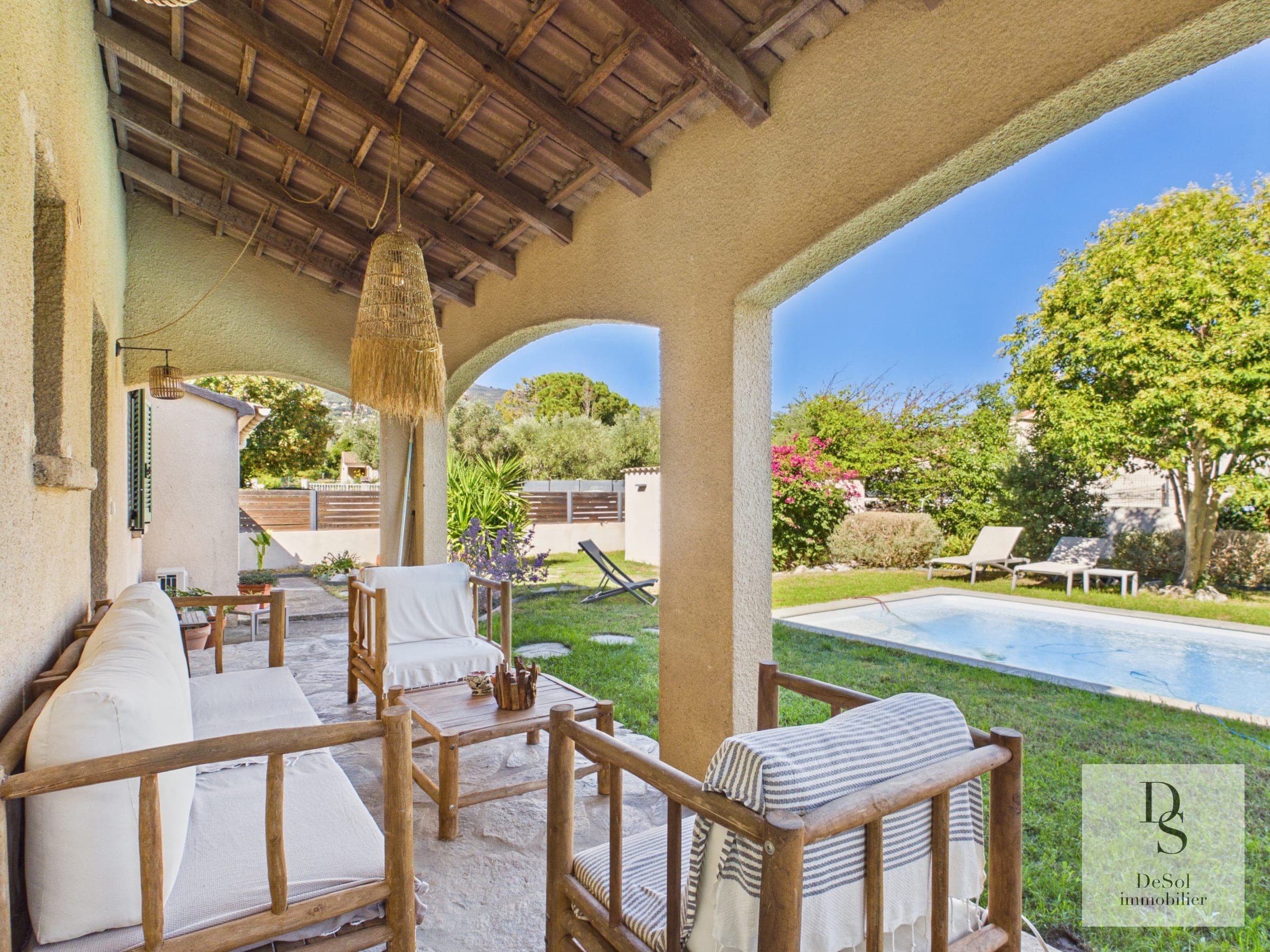 Salon extérieur sous la terrasse couverte, face au jardin et à la piscine